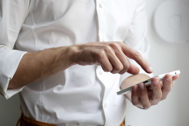 man in white button down texting on smartphone